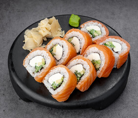 Salmon sushi rolls with cheese. Soft rice rolls with salmon slices and cheese served on a black plate