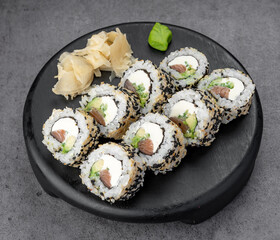 Sesame sushi rolls with salmon. Fresh sesame-coated sushi rolls with salmon and cheese on black plate