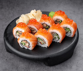 Salmon rolls topped with caviar. Salmon rolls with fish roe topping served fresh on a black round plate