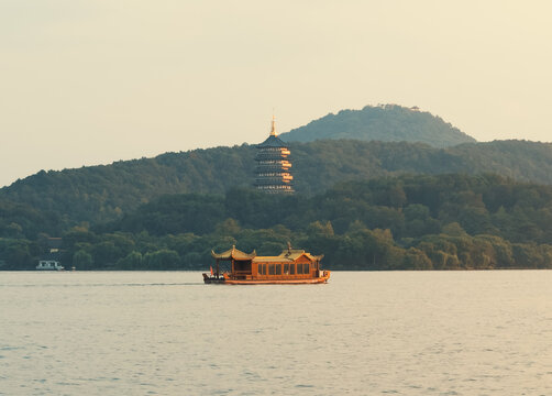 Wooden tourist boat navigate west lake in Hangzhou, China near pagoda temple on hill at dusk