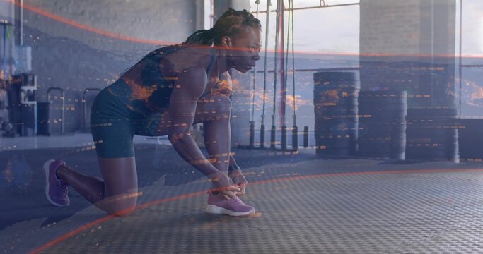 Kneeling woman in dark athletic gear tying purple running shoe on rubber gym mat, digital overlay