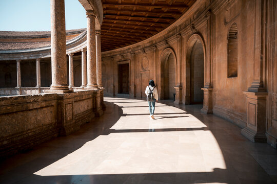 Woman walking in historic palace corridor with sunlight