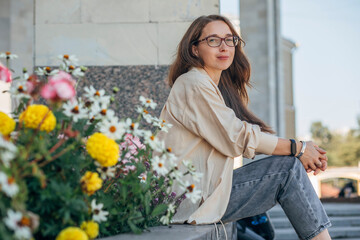 Woman with glasses sitting by city flowers, relaxed outdoor portrait