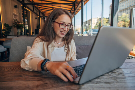 Smiling woman with glasses working on laptop in modern cafe