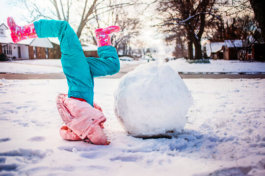 Girl upside down next to giant snowball