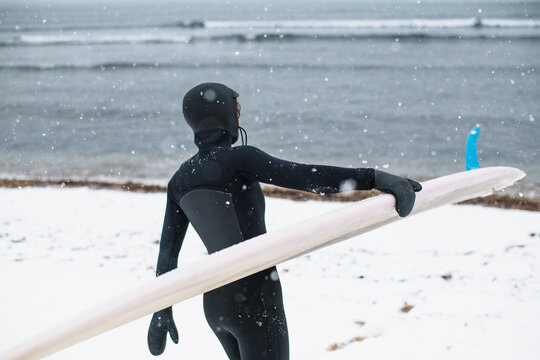 Solo Woman with surfboard on a snowy beach