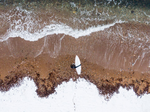 Solo Woman with surfboard on a snowy beach