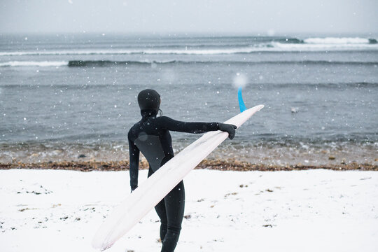 Solo Woman with surfboard on a snowy beach