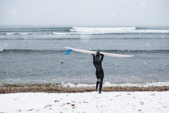 Solo Woman with surfboard on a snowy beach