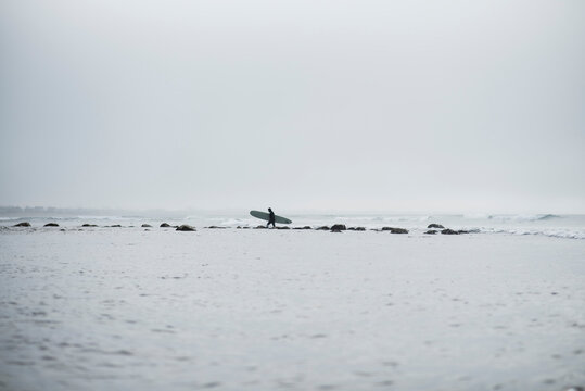 Solo surfer walking shallow shore in winter