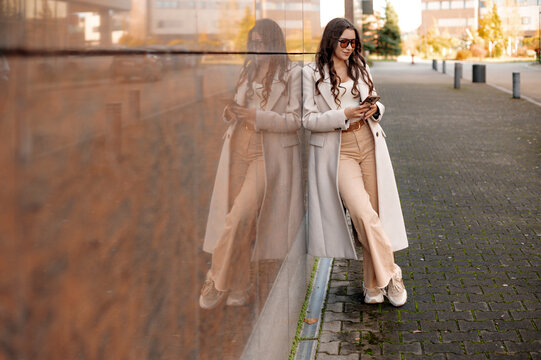 Stylish Woman Using Smartphone by Reflective Wall
