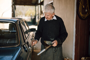 Elderly man checks oil levels in a classic car in a rural workshop