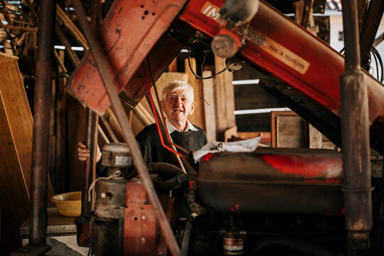 Elderly man working on a vintage tractor in his rustic workshop