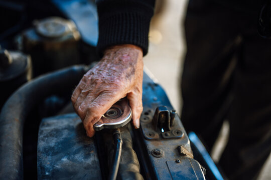 Elderly person performing maintenance on a car engine