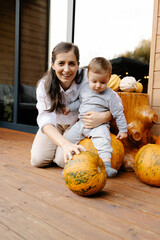 Fototapeta premium Mother and baby celebrating autumn with pumpkins on porch