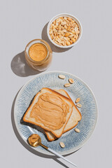 Peanut butter toast on a plate on a blue background with jar of spread, nuts, spoon