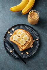 Peanut butter toast and banana on a black plate on a dark background with nuts