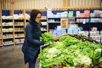 Woman selecting fresh lettuce in supermarket produce section