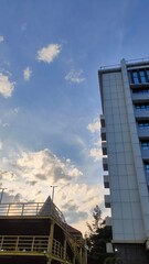 Obraz premium A tall white building stands against a bright blue sky filled with soft clouds. The warm light of the afternoon sun creates a peaceful and calming atmosphere.