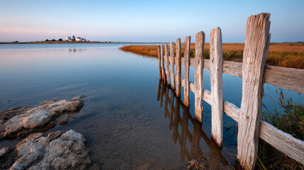 Wooden fence along a calm lake at sunset with distant horizon.