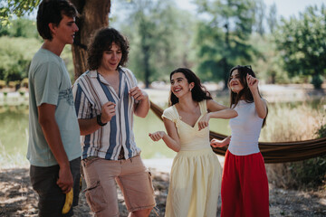 Four young friends share a playful moment outdoors by a calm lake, smiling and dancing. Casual summer outfits and a hammock in the background create a carefree, sociable vibe.