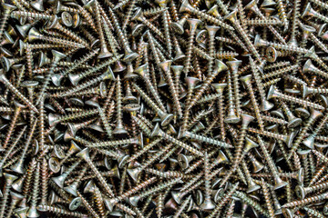 Many golden metal self tapping screws for construction work, closeup, top view. New metal fasteners self tapping screws for connecting wooden elements. Background and texture of metal screws