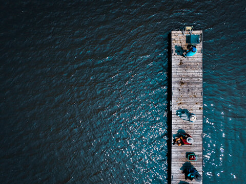 Aerial view of a weathered wooden pier extending into the dark, rippling water, contrasting with the bright sunlight reflecting off the surface, Montreal, Quebec, Canada.