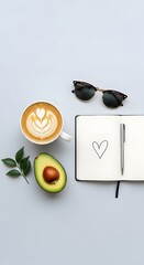 A flat lay of a coffee cup with latte art, sunglasses, a notebook with a heart drawing, an avocado, and a small plant on a light blue background