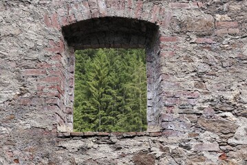 Fototapeta premium A window without glass in an old brick wall, offering a view of the forest.