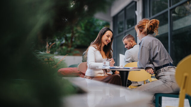 Three people enjoy a casual outdoor cafe scene, sharing a conversation over coffee. The moment conveys friendly networking, collaboration, and everyday business talk in a modern urban setting.