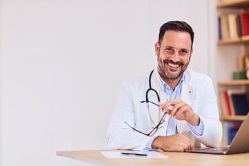 Friendly Doctor With Stethoscope At Desk Smiling At Laptop In Modern Medical Office Today