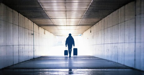 Fototapeta premium Silhouette walks tunnel, carrying luggage. Bright light source creates dramatic perspective, emphasizing solitude, travel.