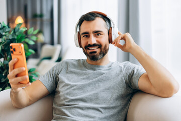 Man wearing headphones listening music on smartphone at home