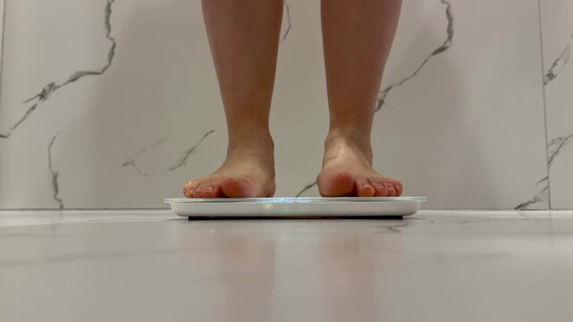 A young girl stands on an electronic floor scale to measure excess weight at home video 4k