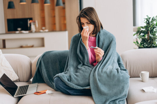 Woman feeling sick checking temperature on couch at home