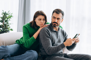Woman feeling jealous of man looking at smartphone
