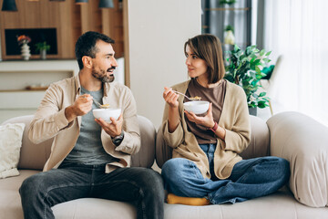 Couple eating breakfast cereal on sofa at home