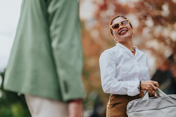 A cheerful woman in a white shirt and sunglasses chats outdoors, carrying a bag during autumn. Bright, friendly scene suitable for topics like collaboration, daily work, and travel.