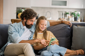 Father and child laughing together using mobile phone on couch