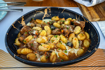 Black decorative plate with gnocchi, lamb cubes,olive, carrot and herb in creamy sauce.
