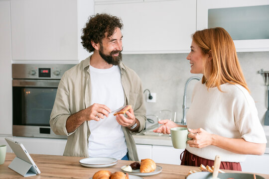 Wife and husband preparing breakfast and talking in kitchen in morning