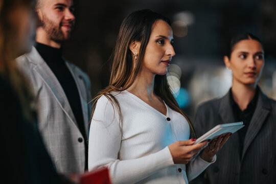 A diverse group of professionals stands in a city setting, focused on a tablet as they collaborate and share ideas. The scene conveys teamwork, networking, and a contemporary business vibe.