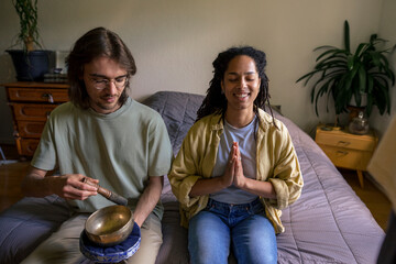 Happy young woman with hands clasped sitting beside friend holding Rin Gong at home
