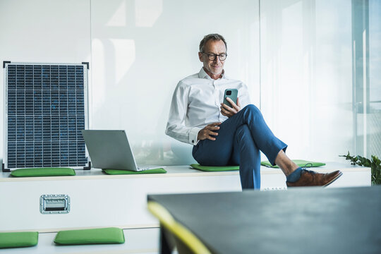 Smiling businessman sitting and using smart phone in office