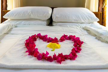 A king-size four-poster bed dressed in white linen is adorned with a heart of bougainvillea petals, celebrating love, romance and new beginnings."