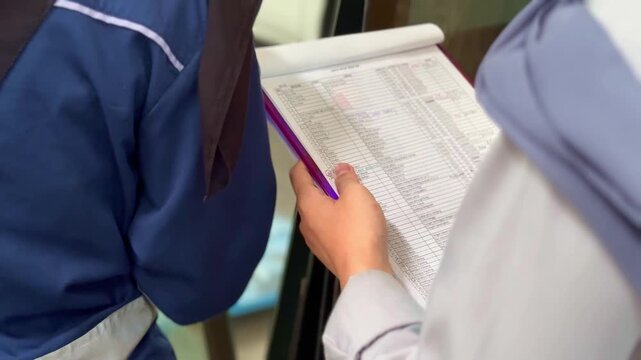 Close-up shot of hands writing and checking documents. Two people filling out paperwork on a clipboard during an administrative process or registration.