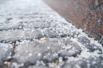 Closeup image of salted paving slabs during winter maintenance,  deicing salt used to reduce slipperiness on roads and sidewalks under freezing conditions. Selective focus