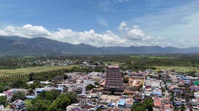 Aerial view of Tenkasi town in Tamil Nadu showcasing the majestic Kasi Viswanathar Temple with lush greenery and the Western Ghats mountains in the background under a bright sky.