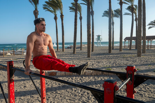 Man performing l sit exercise on parallel bars at beach