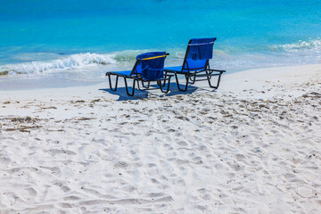 Close up view of two blue lounge chairs with towels on sandy beach on background of Caribbean Sea. Aruba.